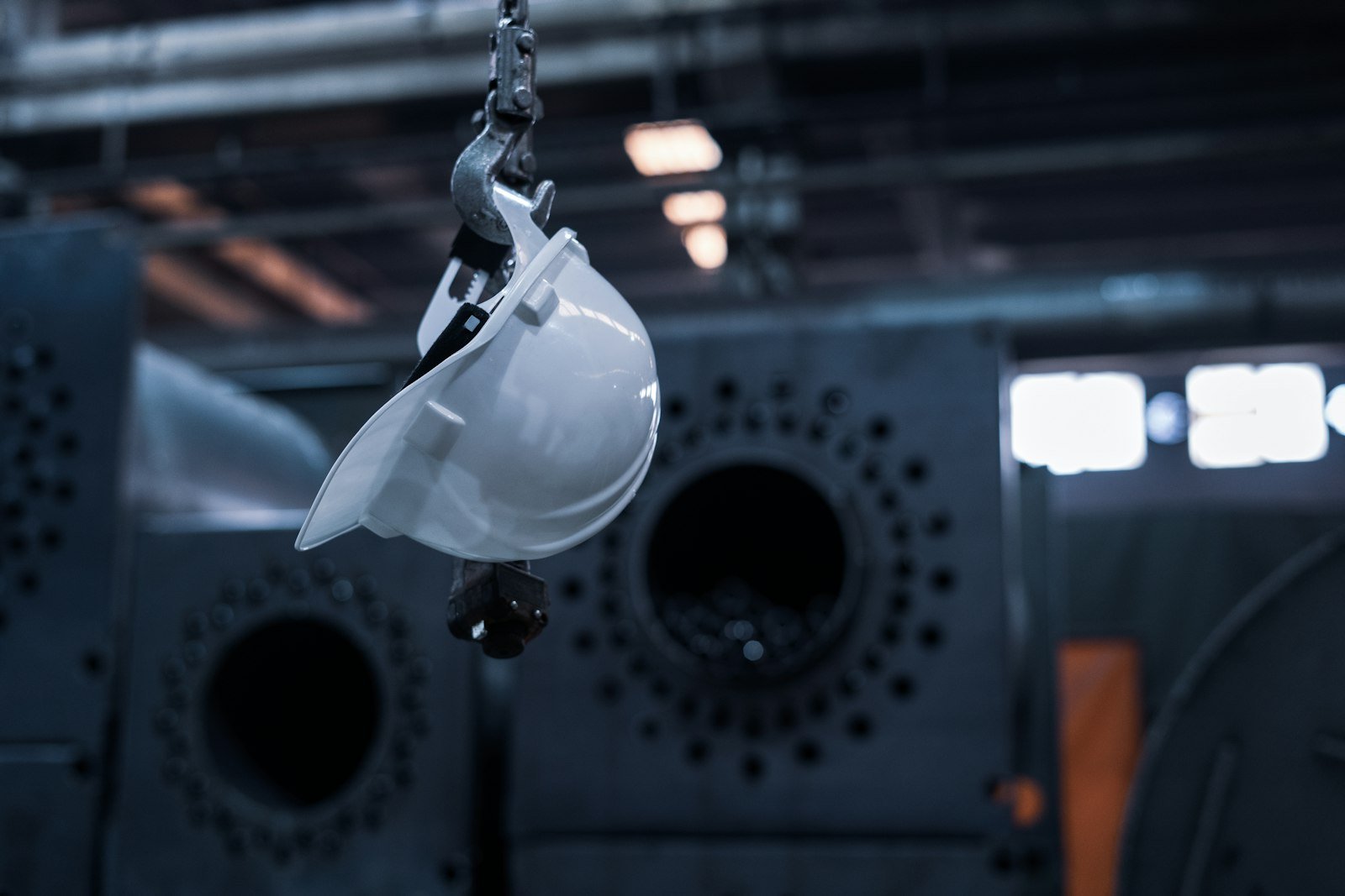 Casco de seguridad blanco colgado de un gancho metálico en una nave industrial oscura
