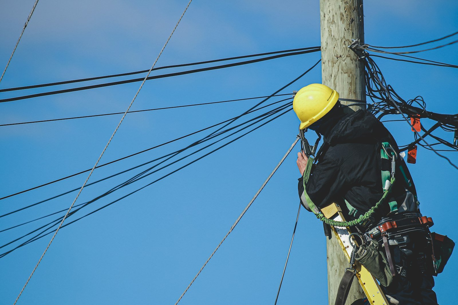 Técnico con casco amarillo trepando un poste de líneas telefónicas