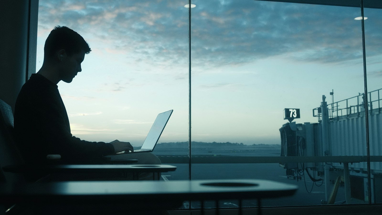 Trabajador con laptop junto a la ventana de un aeropuerto al amanecer
