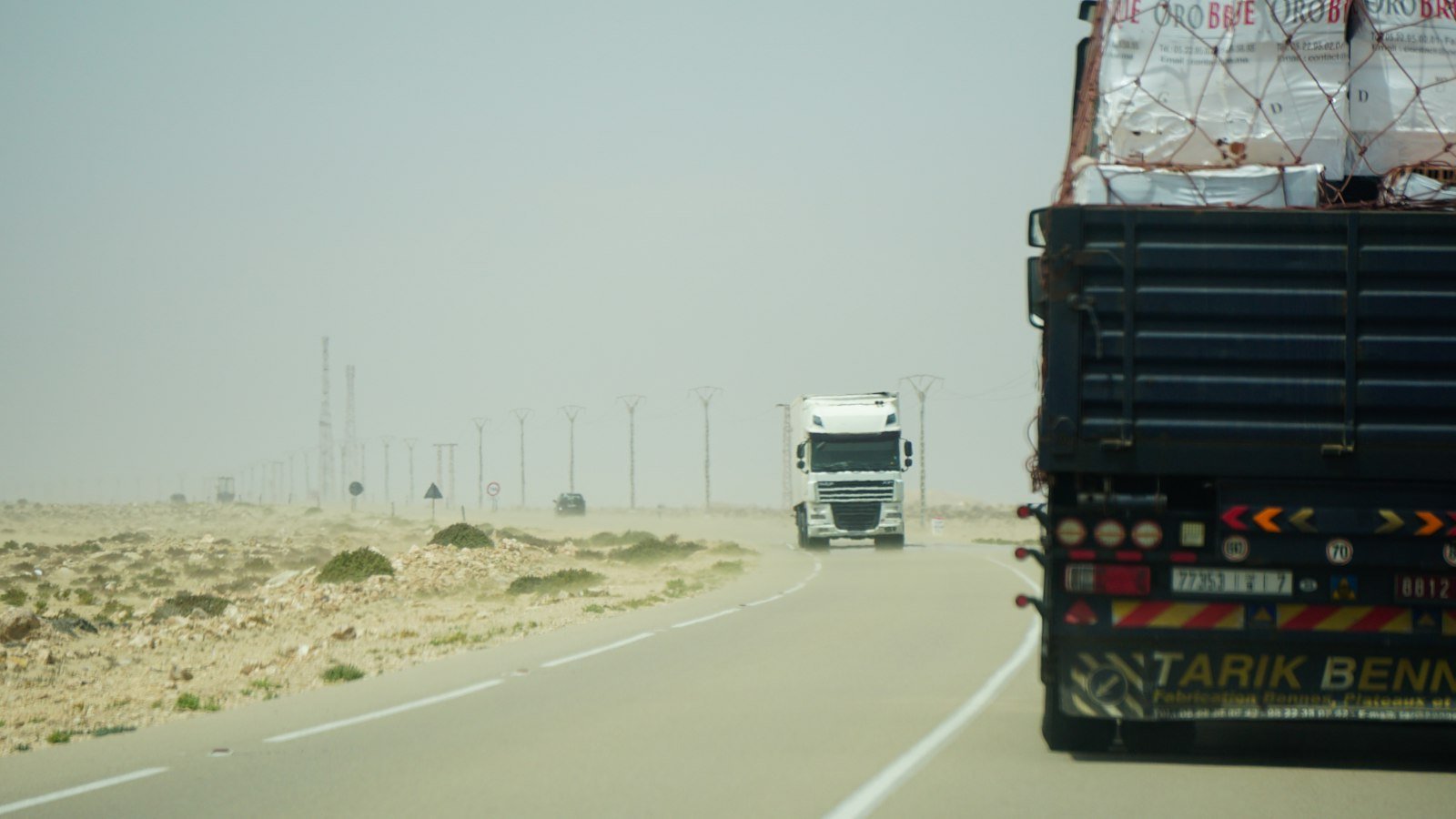 Dos tractocamiones circulan por una carretera desértica bajo un cielo brumoso