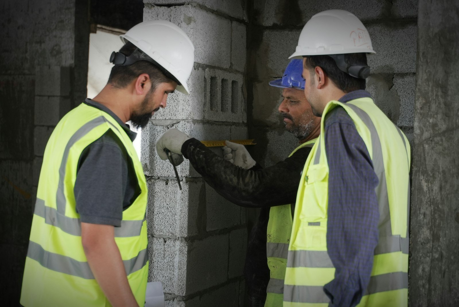 Trabajadores con casco y chaleco midiendo un muro de concreto